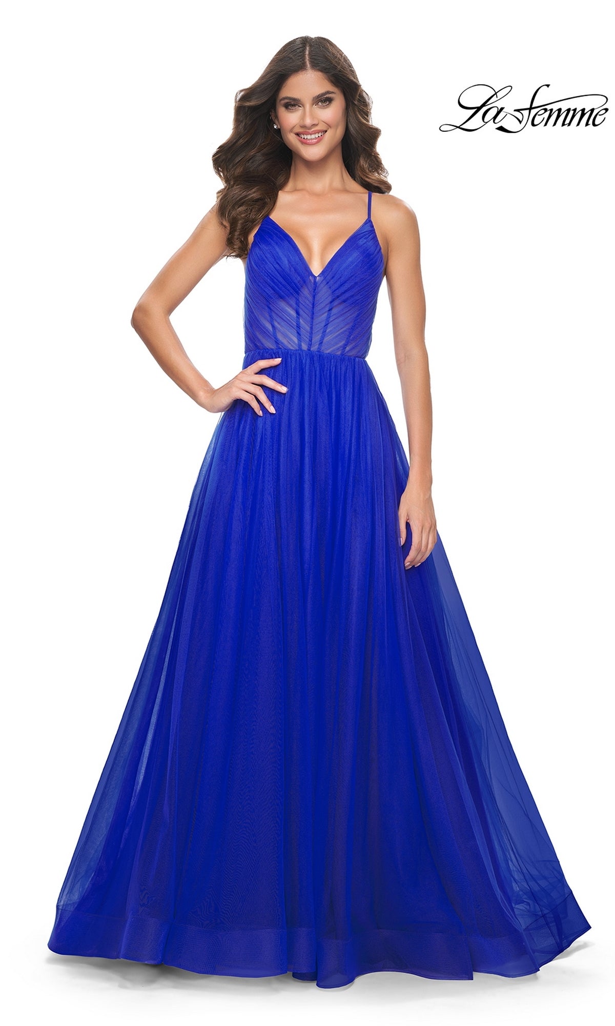 A woman in a royal blue, floor-length La Femme Sheer-Waist Long Prom Ball Gown 31457 with thin straps and fitted bodice stands against a white background. The La Femme logo appears in the top right corner.